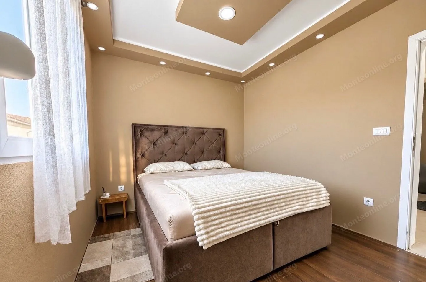 Furnished bedroom with a double bed and a dropped ceiling with lighting.