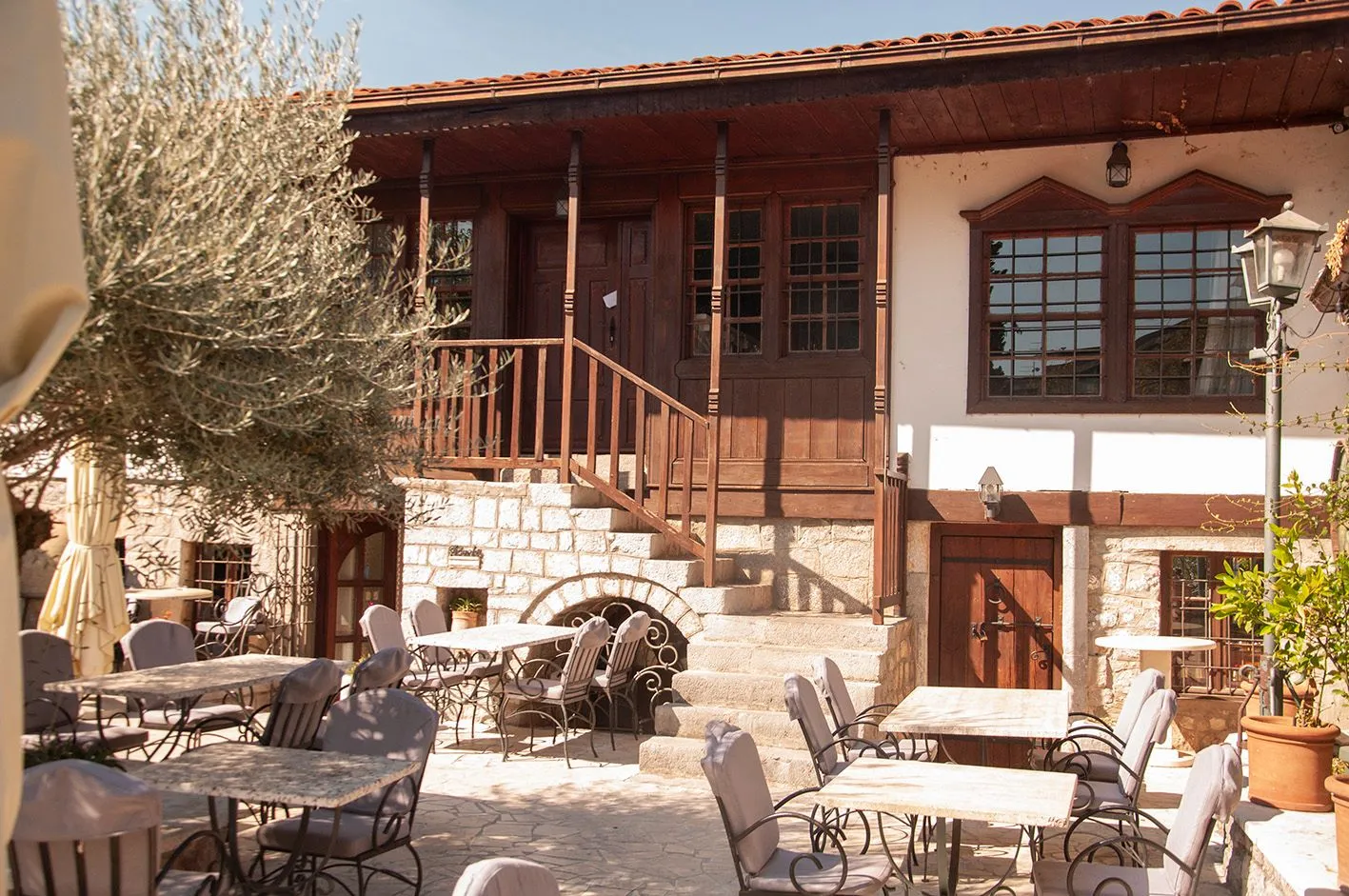 Exterior of a traditional house with a wooden terrace and a paved courtyard with garden tables.