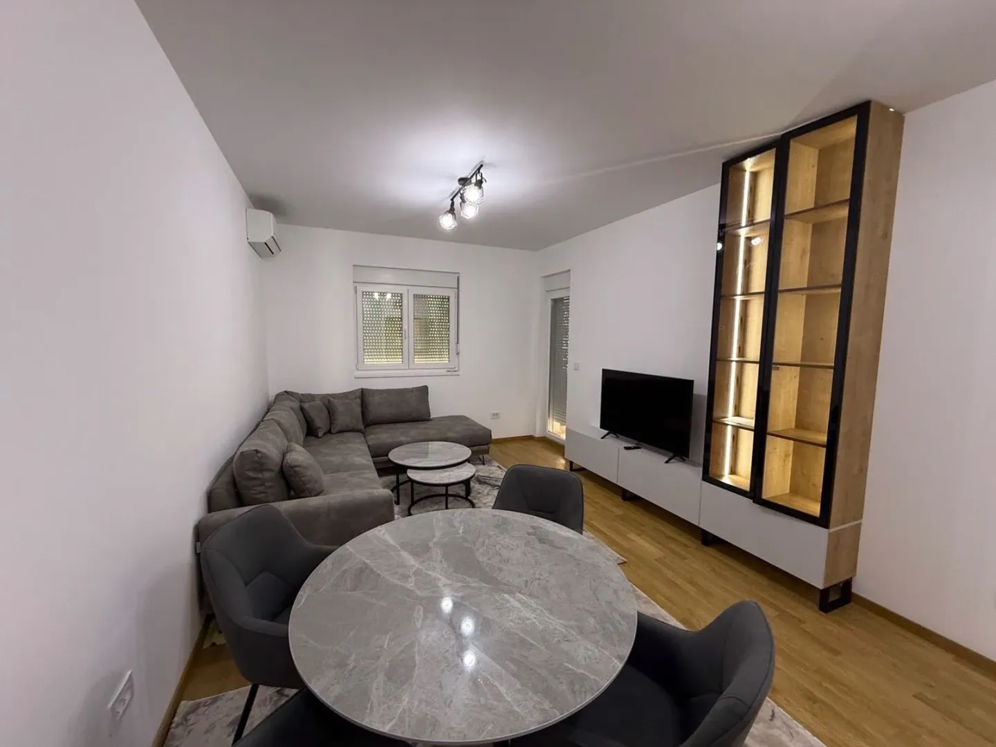 Living room with a sectional sofa, dining table, and TV unit.