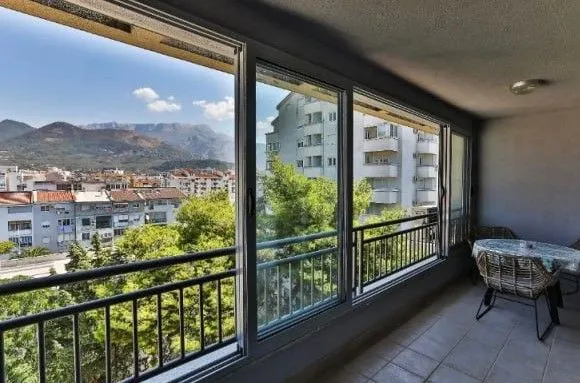 Zastakljeni balkonski prostor sa garniturom za sjedenje i pogledom na grad.