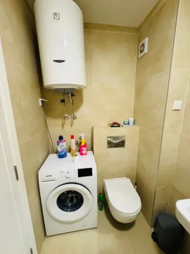 Small bathroom with a toilet, washing machine, and water heater. - image 5