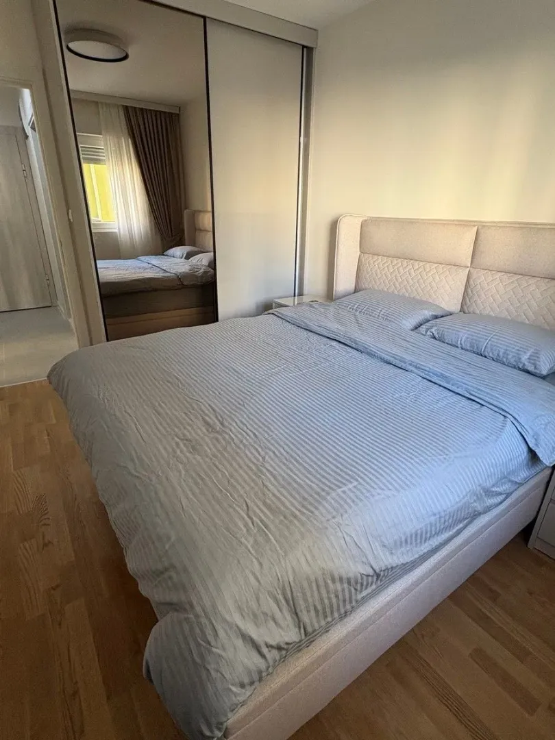 Namještena spavaća soba sa bračnim krevetom i velikim ormarom sa ogledalom.