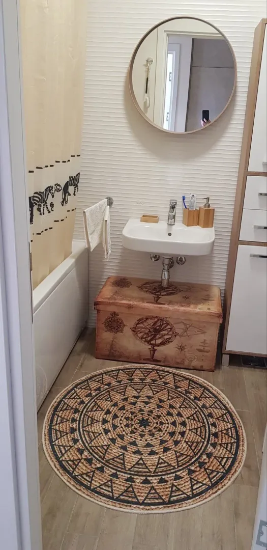 Small bathroom with a sink, round mirror, and a bathtub with a curtain.