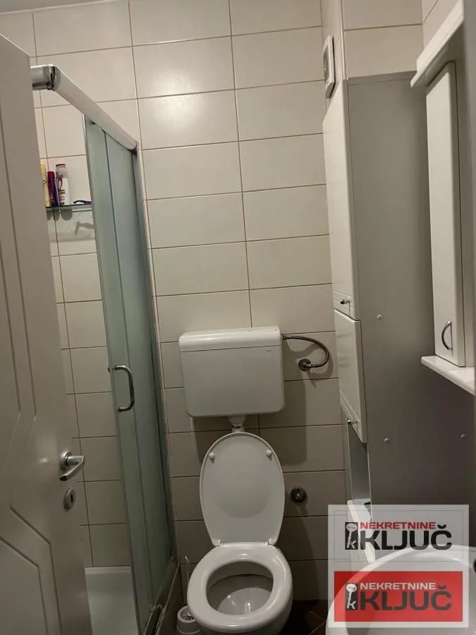 Small bathroom with a toilet, shower cabin, and white cabinet.
