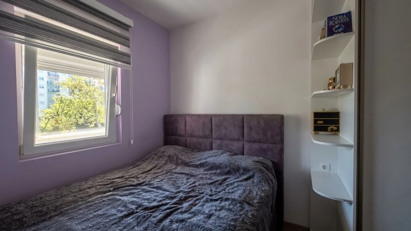 Small bedroom with a double bed, purple wall and a window.