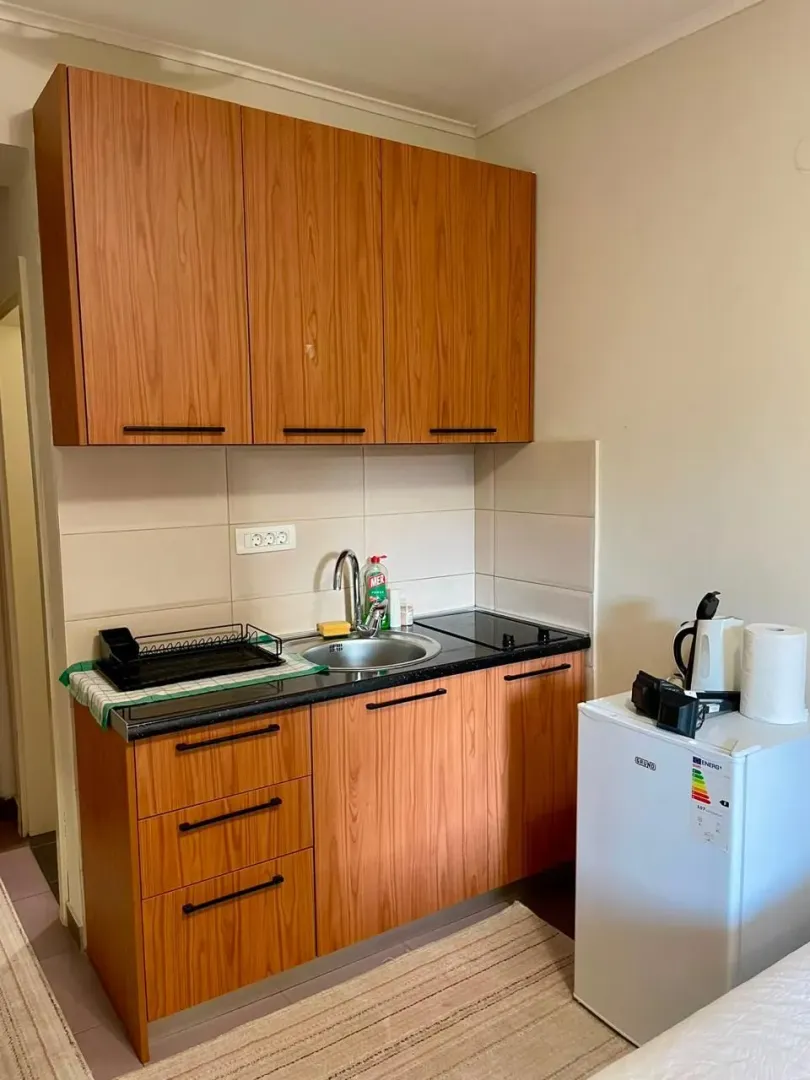 Small kitchen with wooden cabinets, sink, and mini fridge.