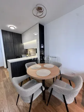 Trpezarija sa okruglim stolom i modernom kuhinjom u pozadini. - image 16