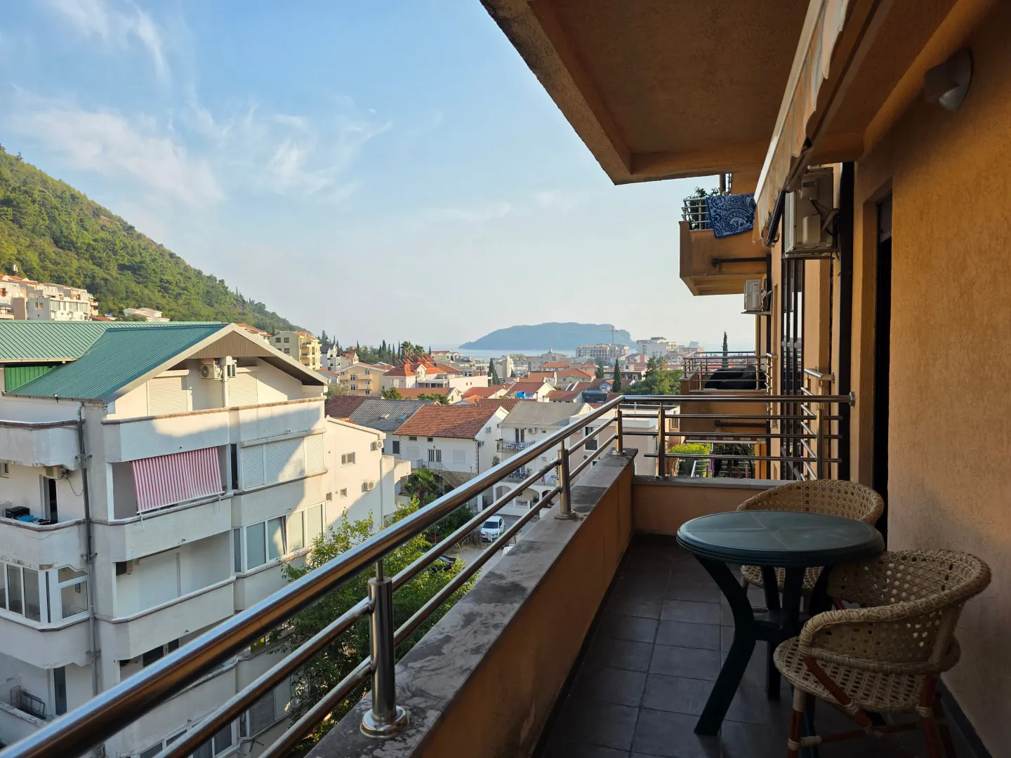 Natkriveni balkon sa garniturom za sjedenje i pogledom na naselje i more.