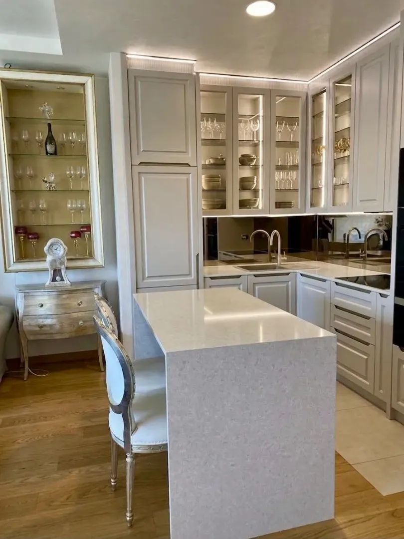 Modern kitchen with white cabinets, an island, and glass display cabinets for drinks.