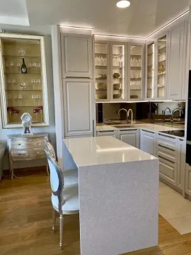 Modern kitchen with white cabinets, an island, and glass display cabinets for drinks. - image 5