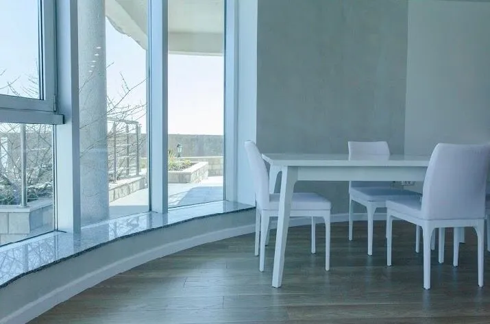 Bright dining area with a white table and chairs next to large windows.