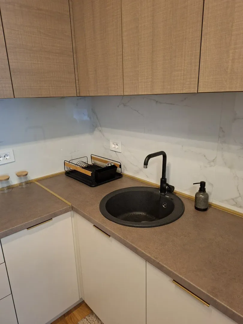 Kitchen countertop with a round black sink and wooden cabinets.
