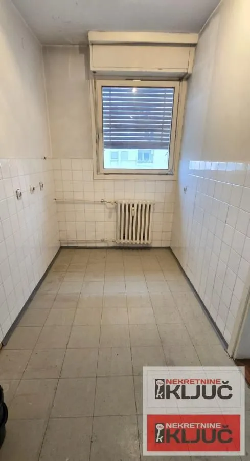 Prazna kuhinja sa pločicama na zidovima i podu i prozorom.
