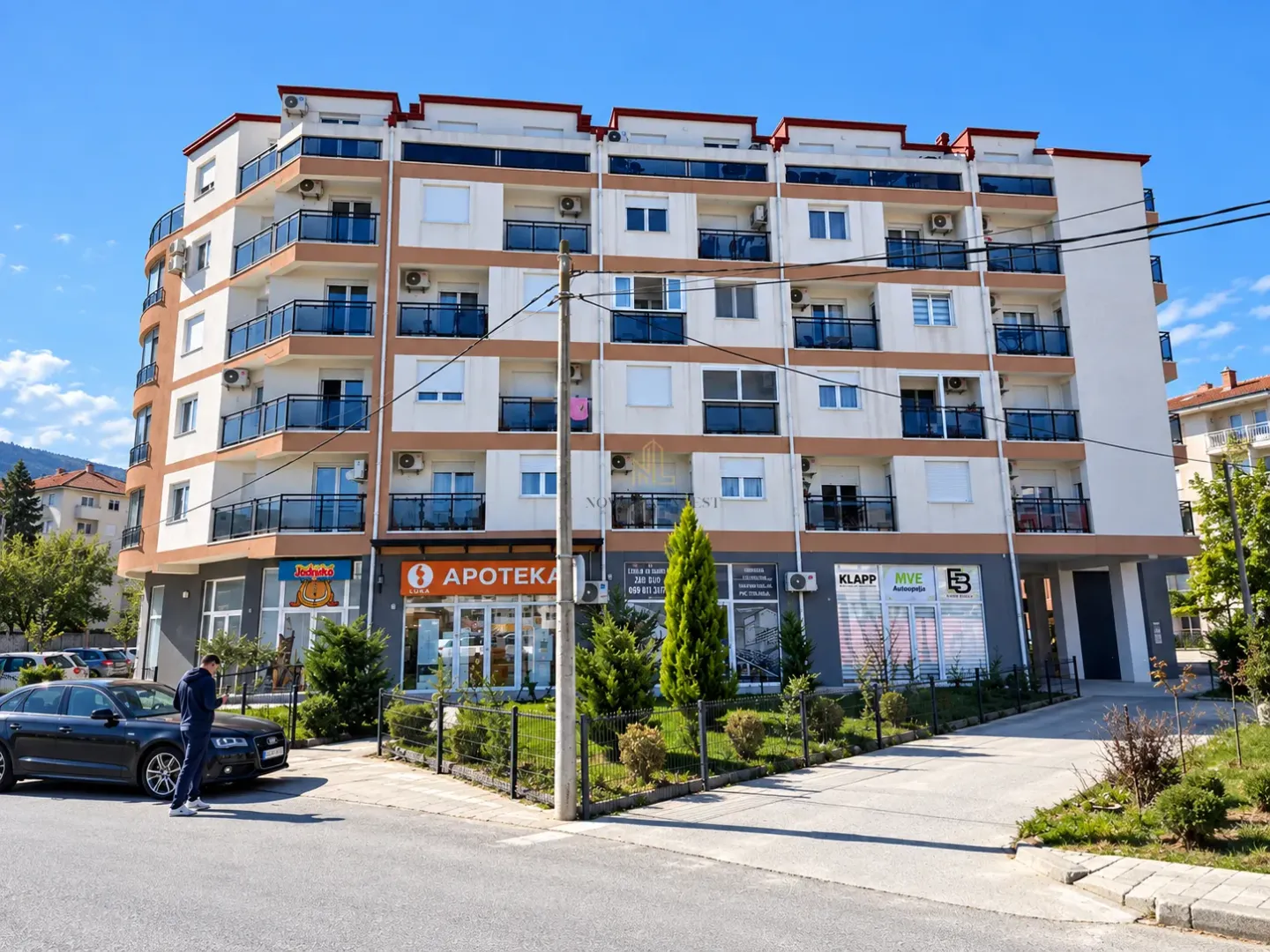 Front view of an apartment building with ground floor commercial spaces and a landscaped yard.