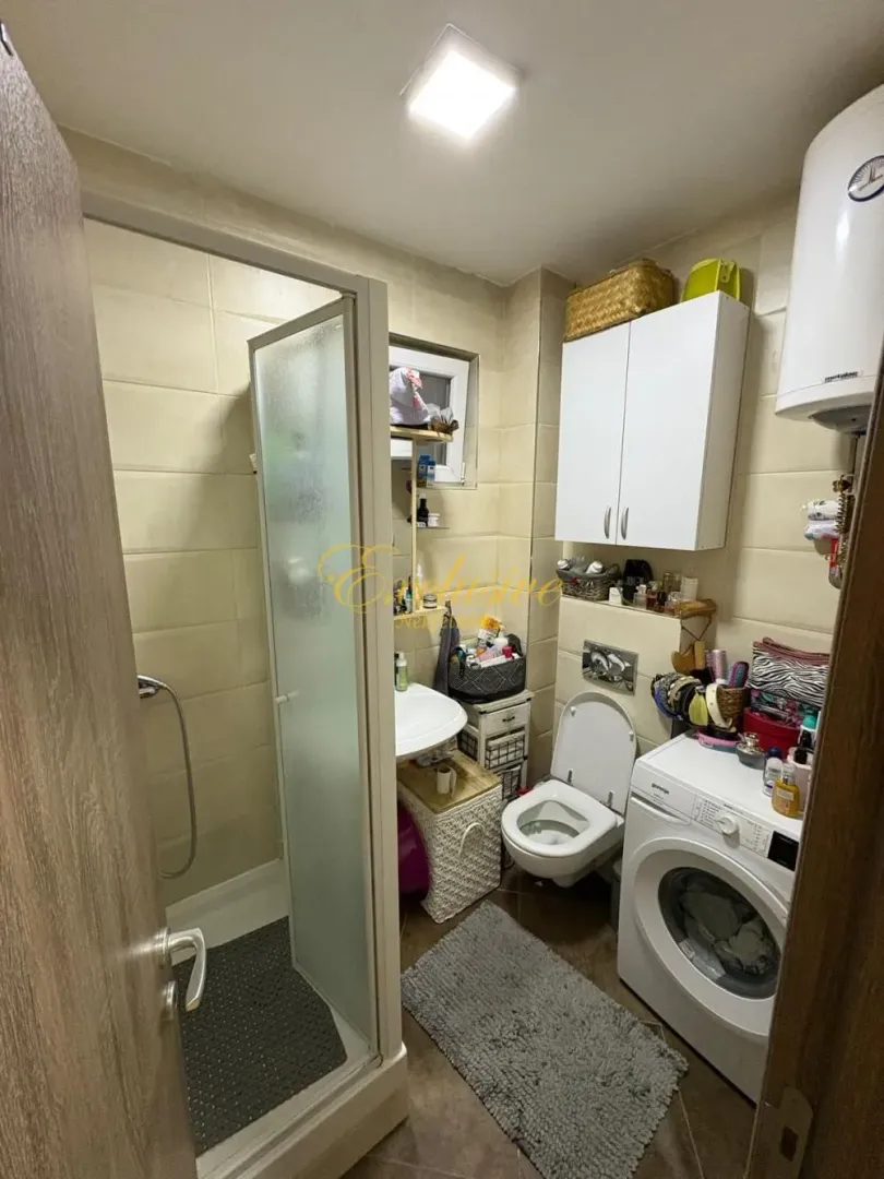 Manje kupatilo sa tuš kabinom, WC šoljom, umivaonikom i mašinom za veš.