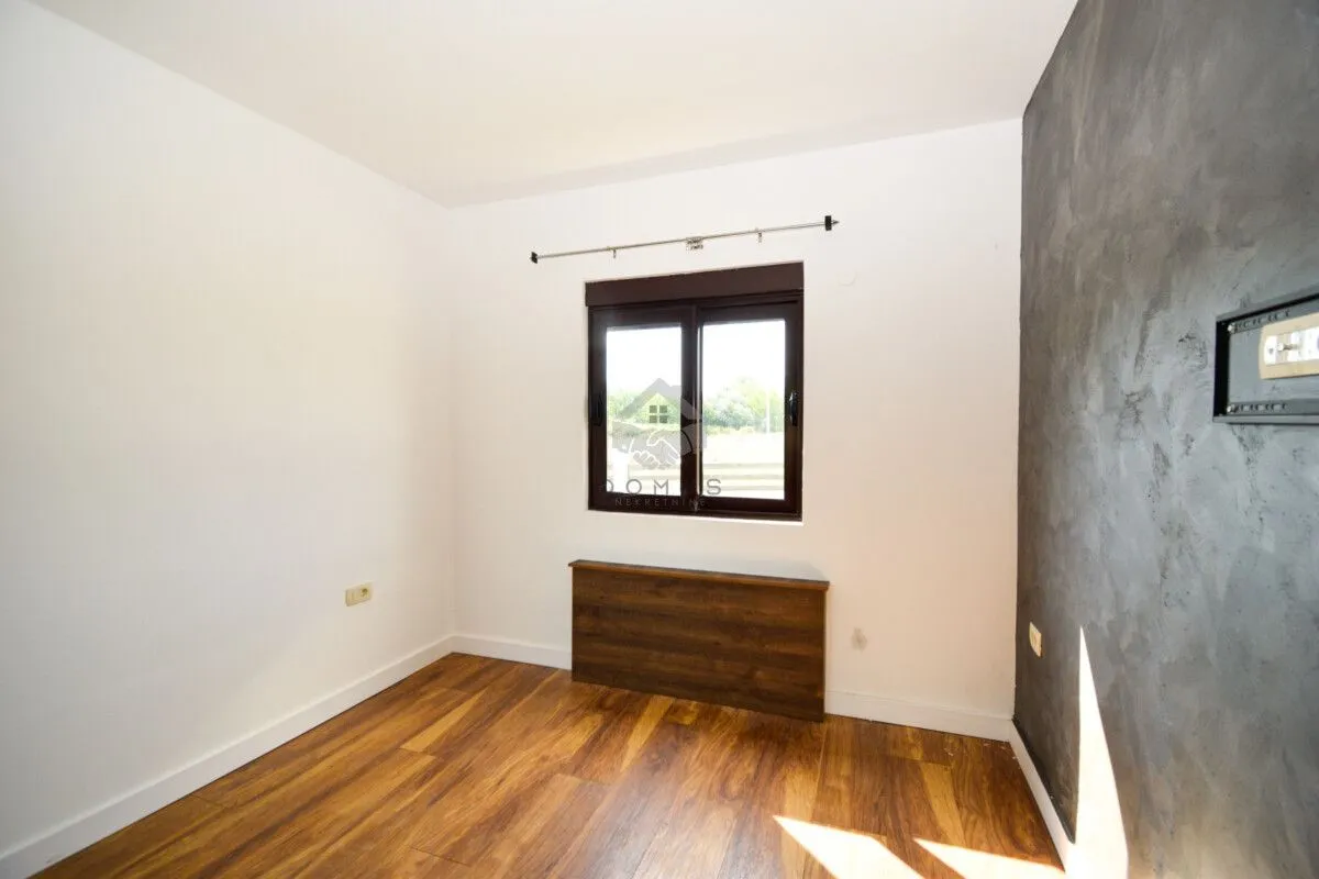 Empty room with wooden flooring, white walls, and a dark accent wall featuring a window.
