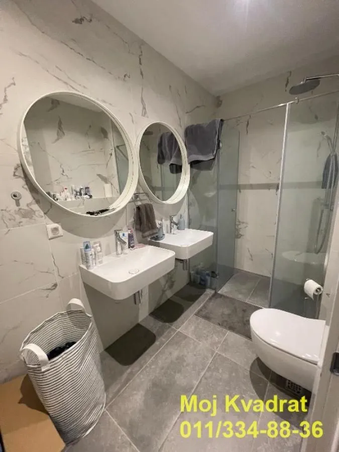 Modern bathroom with two sinks, a walk-in shower, and round mirrors.