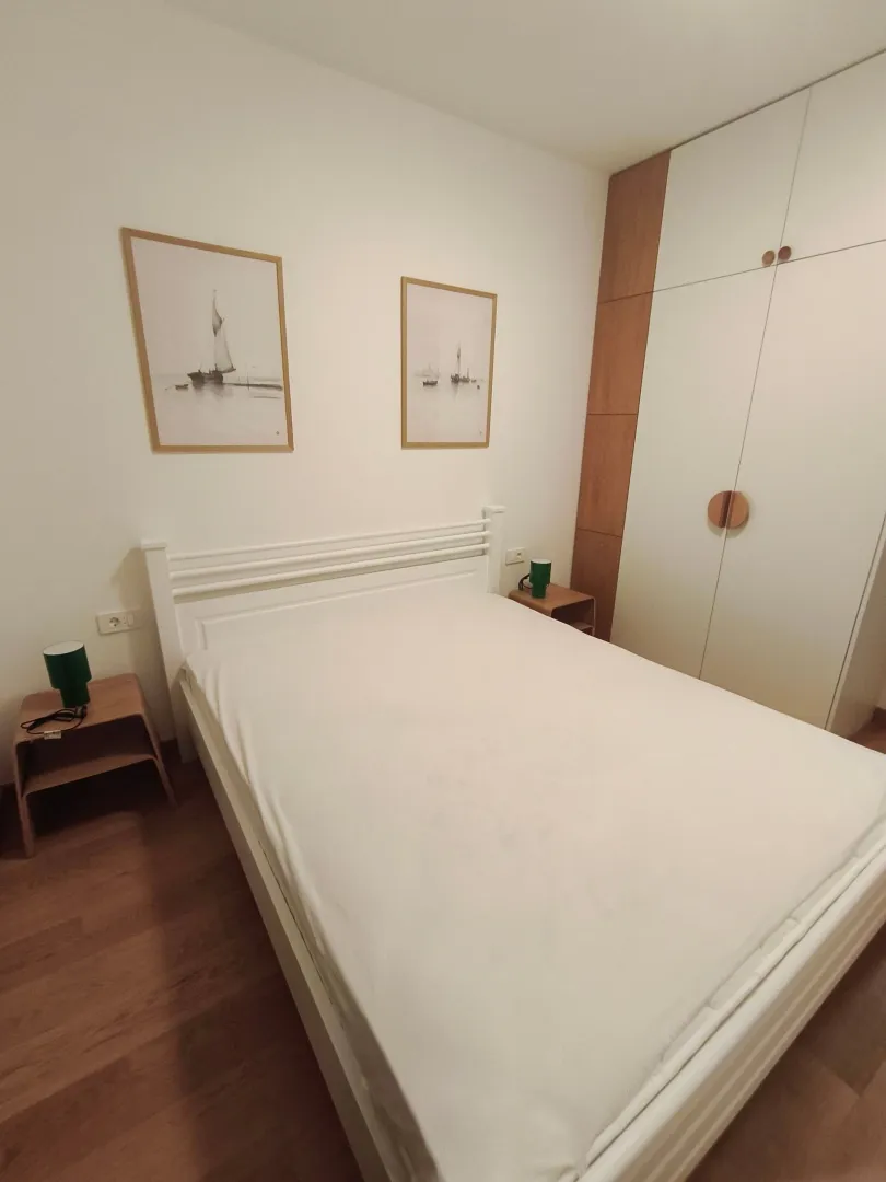 Uređena spavaća soba sa bračnim krevetom, plakarom i noćnim stočićima.