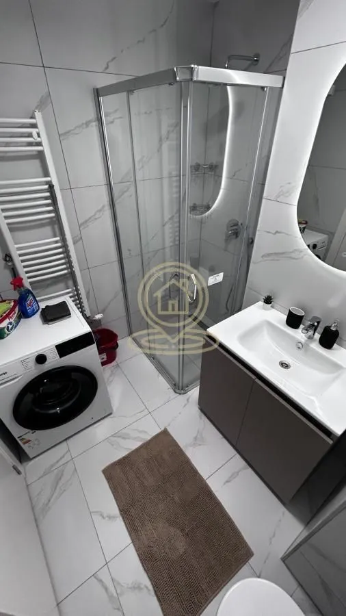 Modern bathroom with a shower cabin, washbasin, and washing machine.