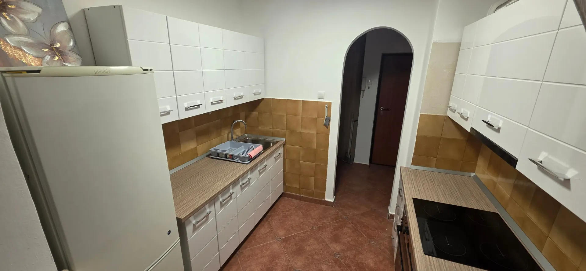 Manja kuhinja sa bijelim elementima, sudoperom i ugrađenom pločom za kuvanje.