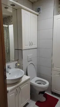 Small bathroom with a sink, toilet, and white cabinets. - image 2