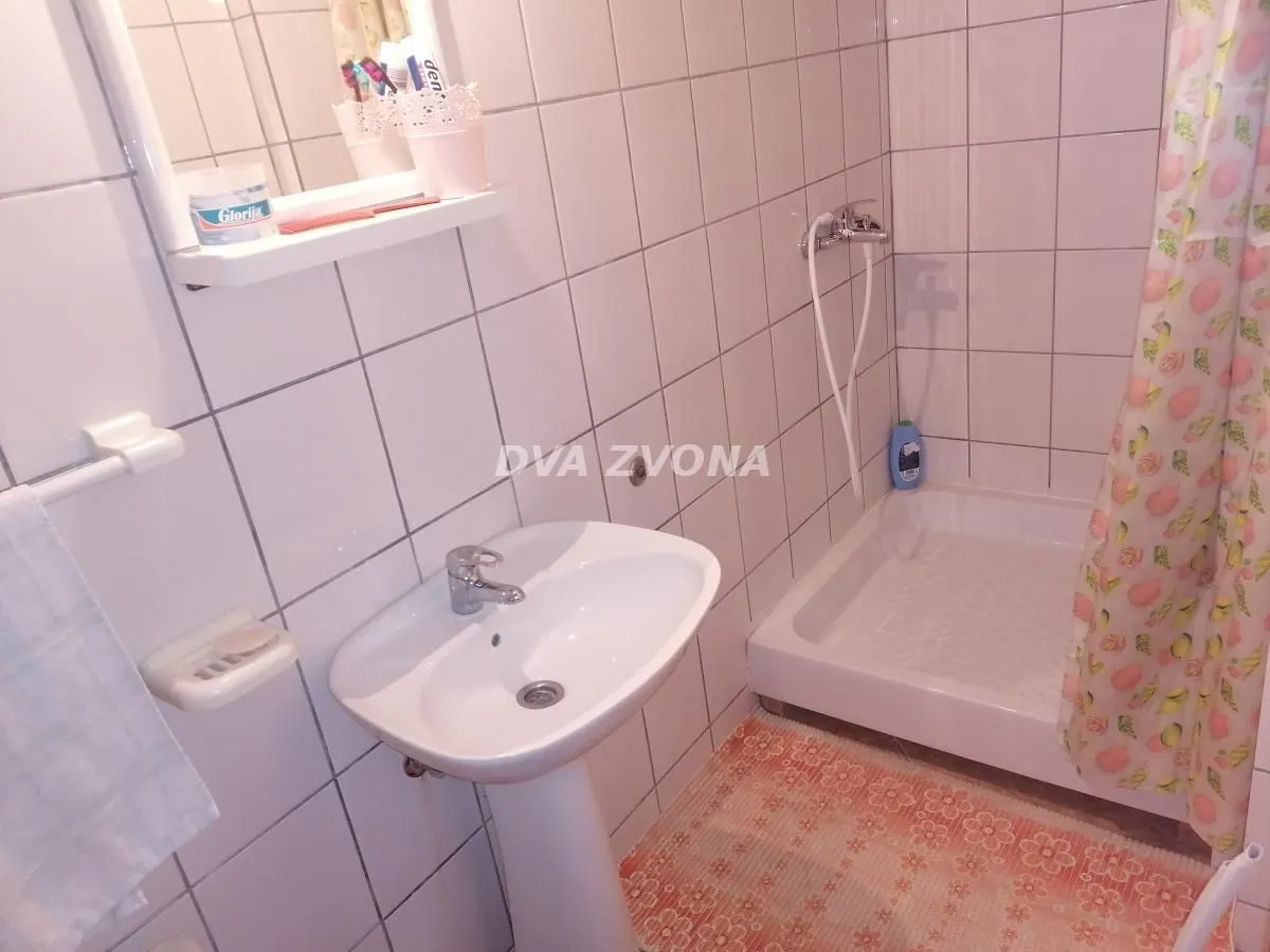 Small bathroom with a sink, shower cabin, and white tiles.