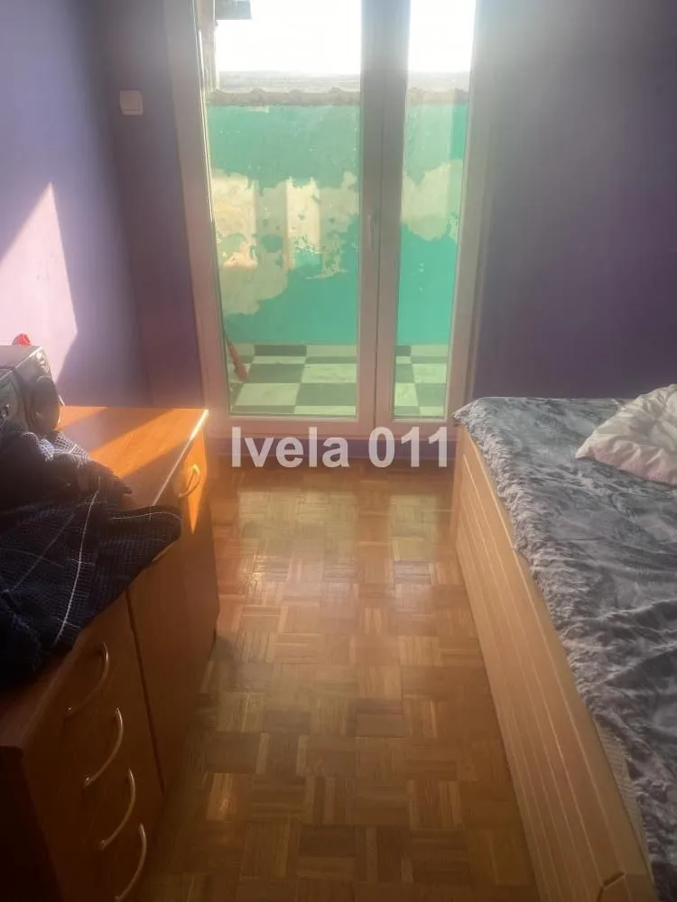 Spavaća soba sa krevetom, komodom i balkonskim vratima.