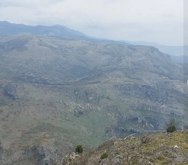 Panoramski pogled na planinski predio pod oblačnim nebom.
