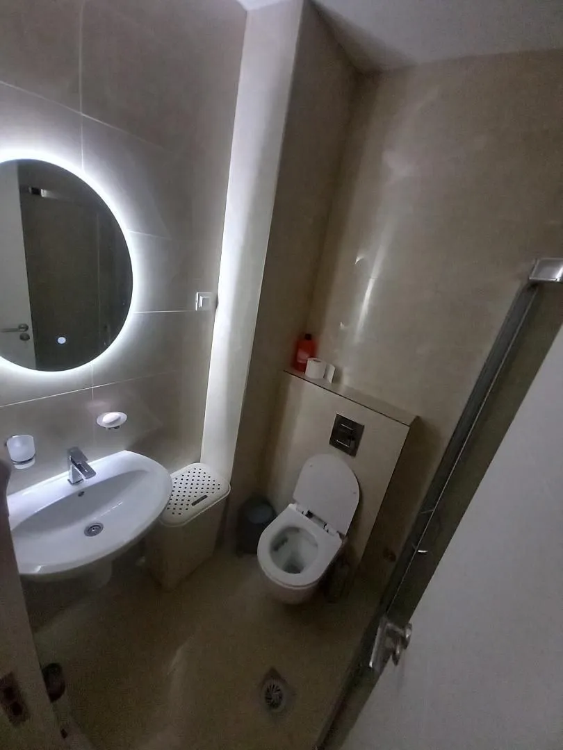 Modern bathroom with sink, toilet, and illuminated mirror.