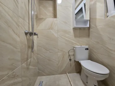 Compact bathroom tiled in beige with a walk-in shower and toilet. - image 12