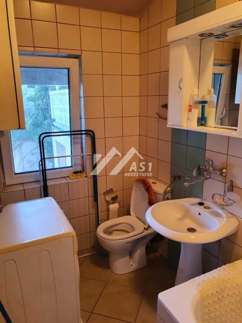 Manje kupatilo sa umivaonikom, WC šoljom, mašinom za veš i prozorom.