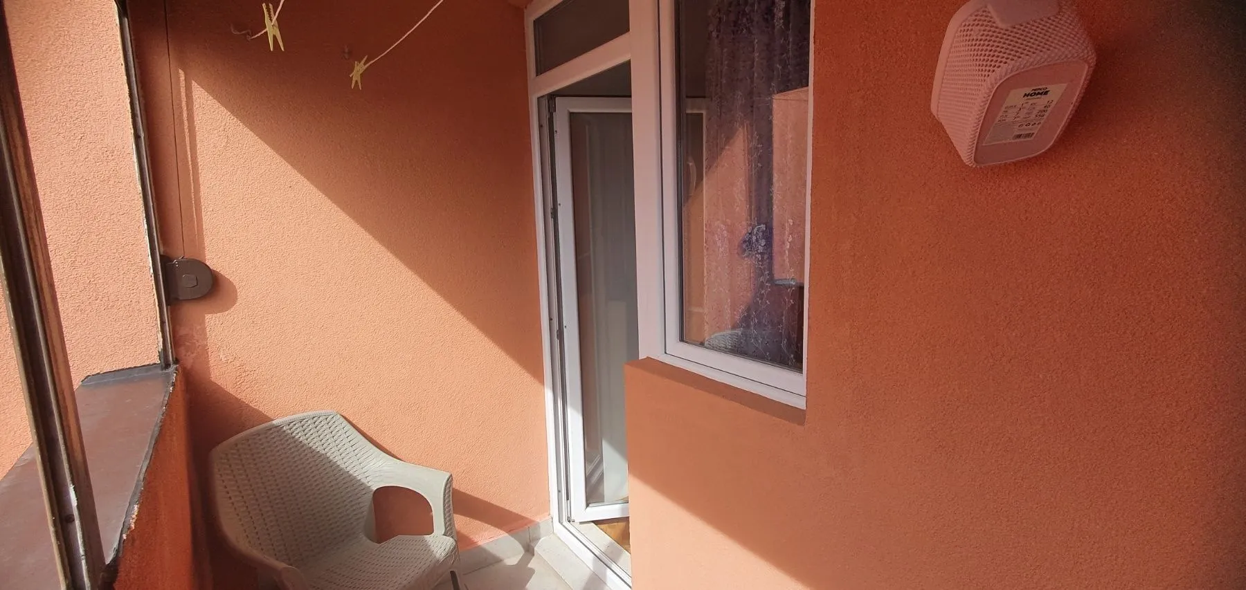 Mali balkon sa plastičnom stolicom i narandžastim zidovima.