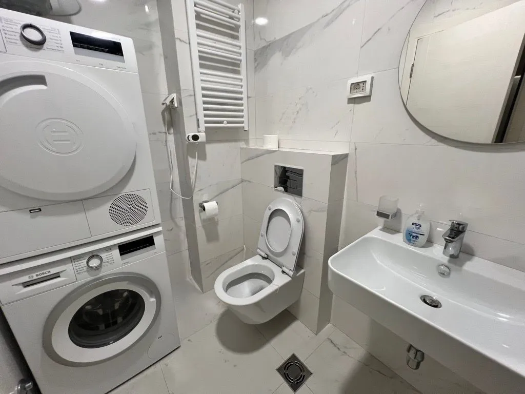 Moderno opremljeno kupatilo sa bijelim pločicama, sanitarijama i ugrađenom mašinom za veš.
