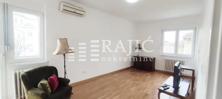 Spacious living room with wooden flooring, an armchair, and a television.