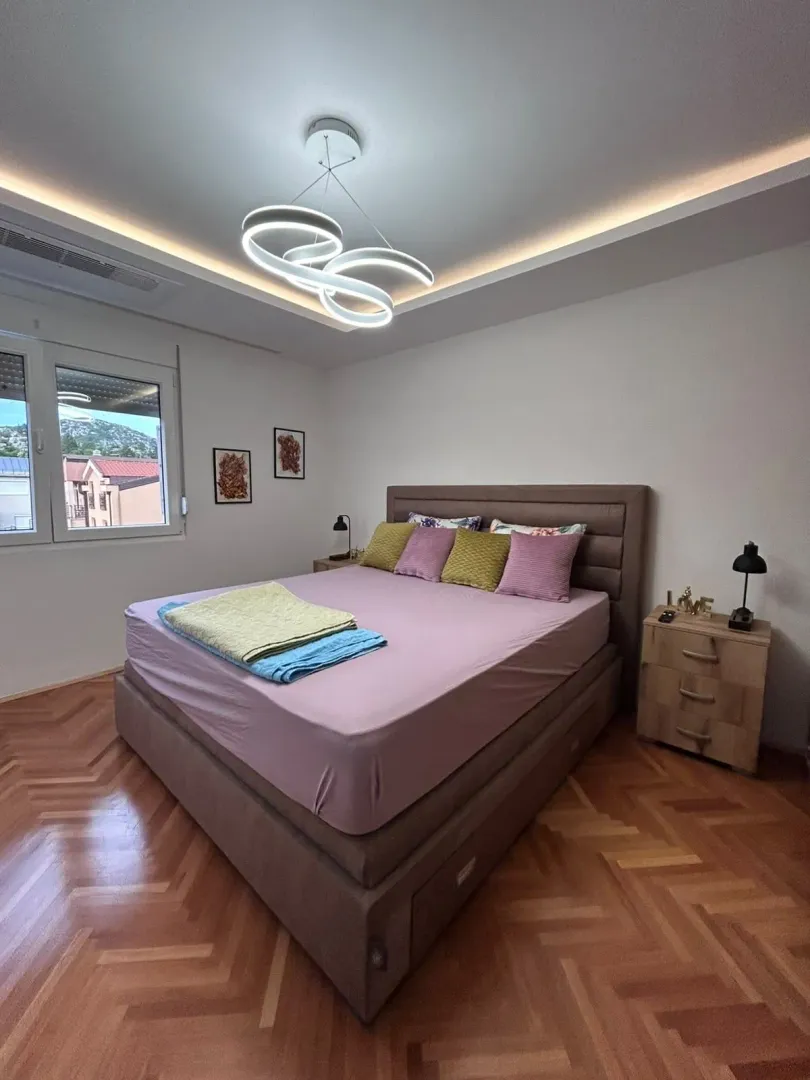 Modern bedroom with a double bed, parquet flooring, and decorative lighting.