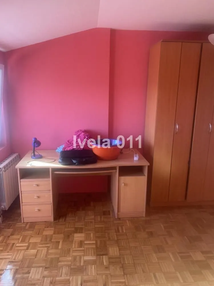 Manja spavaća soba sa roze zidom, drvenim radnim stolom i ormarom.