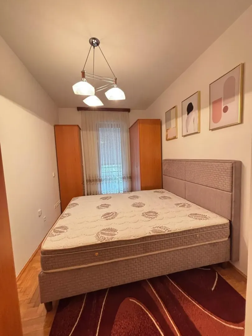 Svijetla spavaća soba sa bračnim krevetom i dva ormara pored prozora.