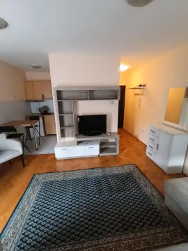 Living room with a TV set, a rug, and a view of the kitchen in the background. - image 2