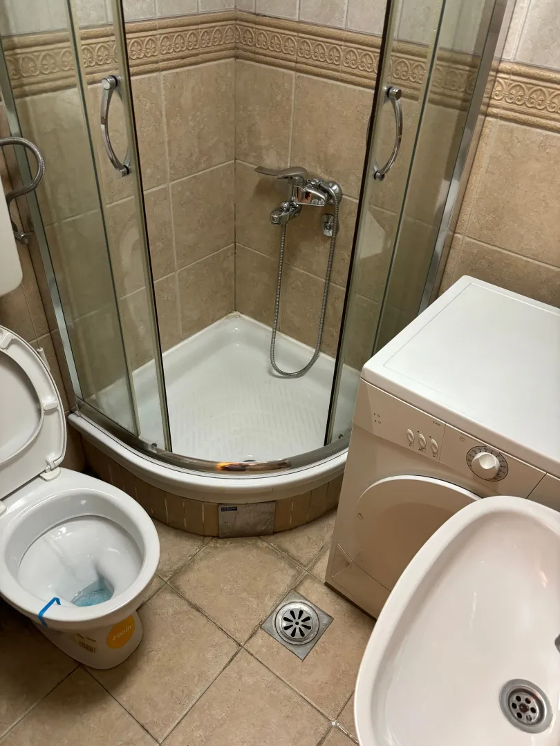 Manje kupatilo sa tuš kabinom, WC šoljom i veš mašinom.