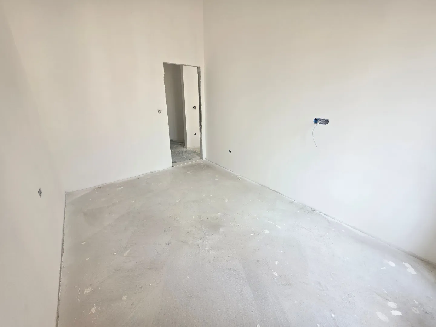 Prazna prostorija u novogradnji sa bijelim zidovima i betonskim podom.