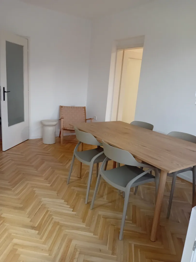 Trpezarija sa drvenim stolom i stolicama u svadjenom enterijeru.