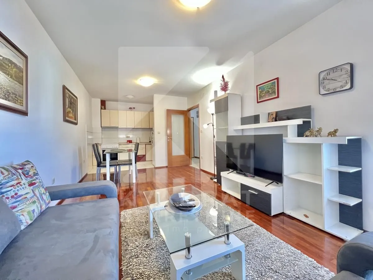 Living room with a sofa, TV unit, and a dining area in the background.