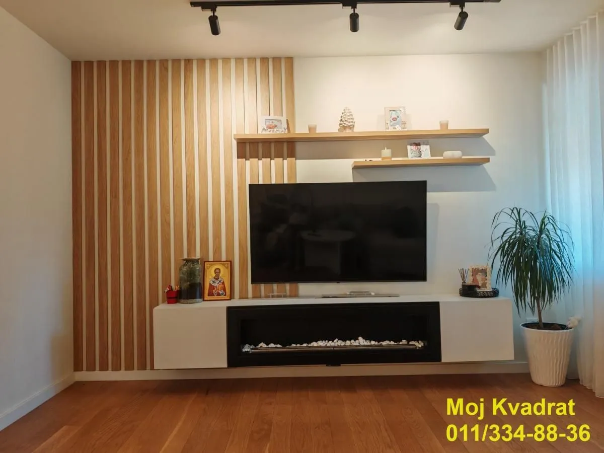 Dnevna soba sa TV policom i drvenim dekorativnim panelima na zidu.