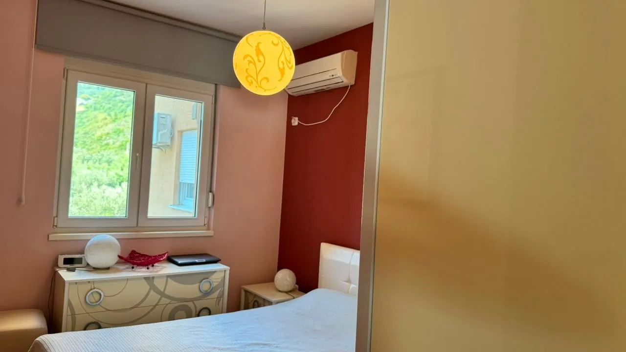 Manja spavaća soba sa bračnim krevetom, komodom i prozorom koji gleda na zelenilo.