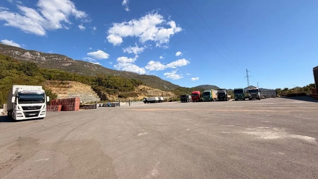 View of a spacious open plot with parked trucks and hills in the background.