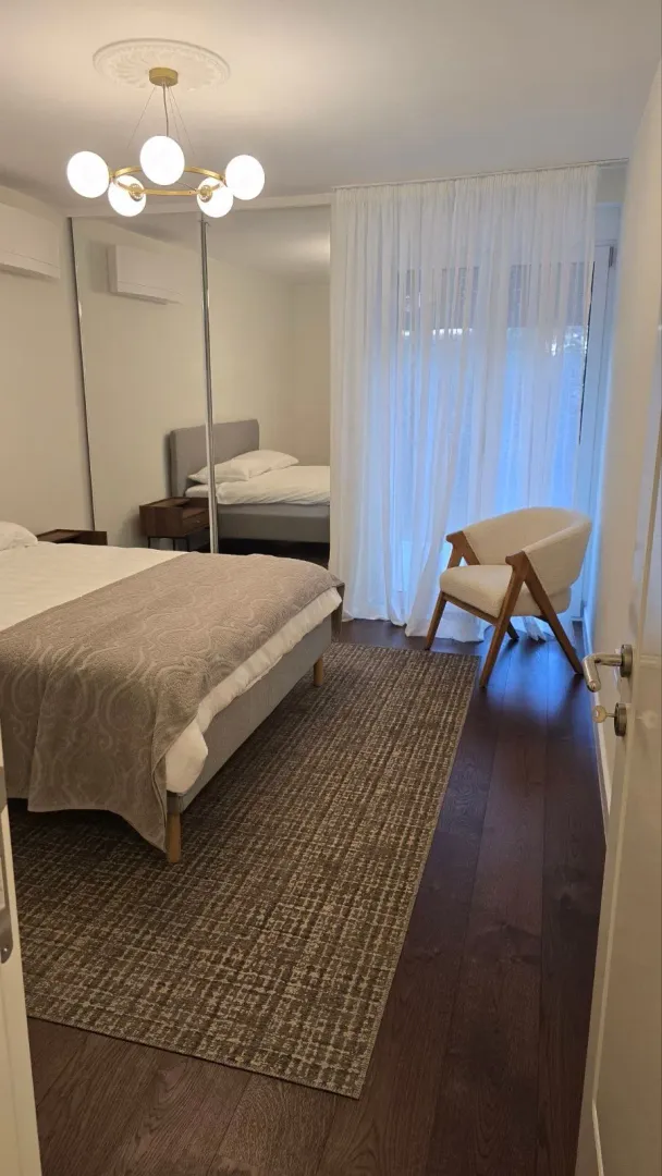 Modern bedroom with a double bed, mirrored wardrobe, and an armchair.