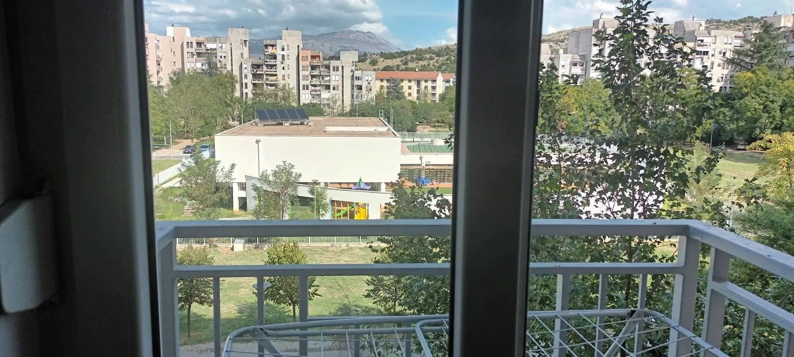Pogled sa balkona na park i okolne zgrade.