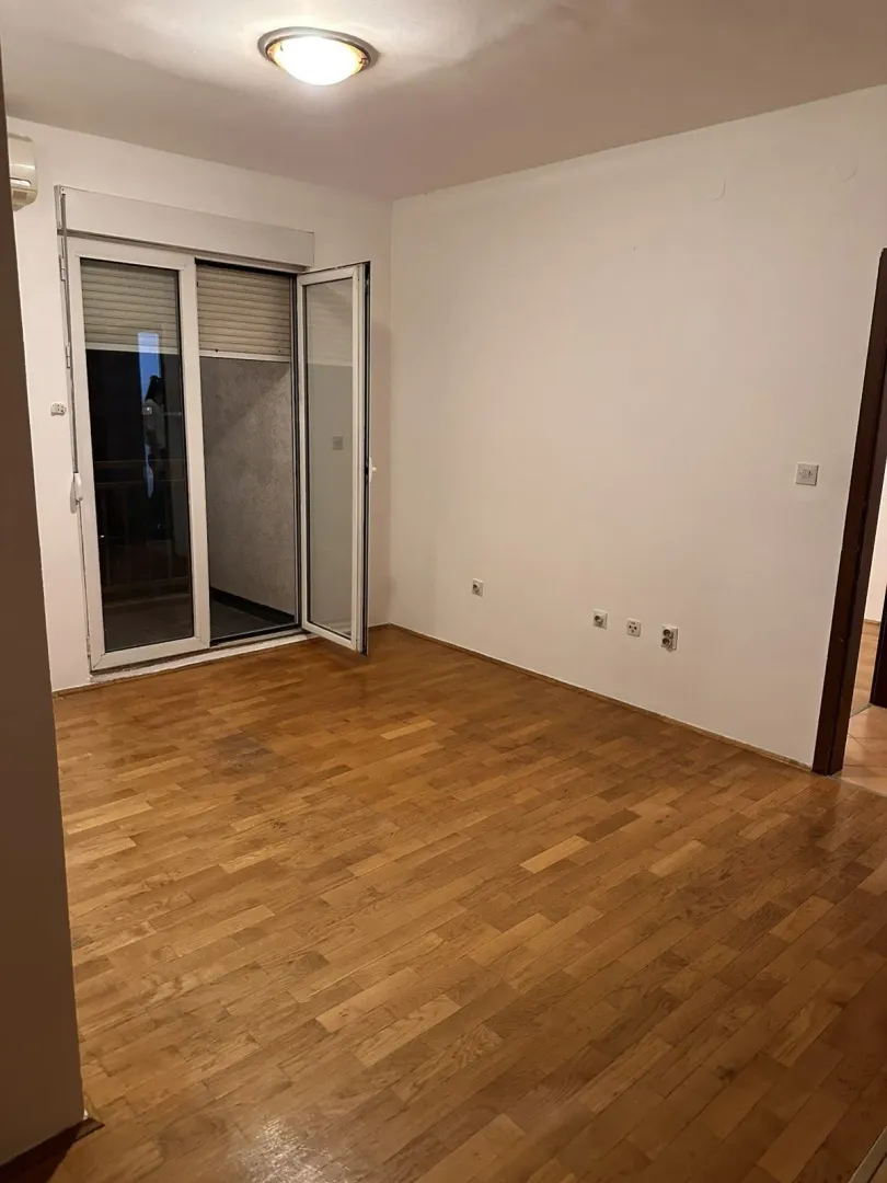 An empty room with wooden parquet flooring and an open balcony door.