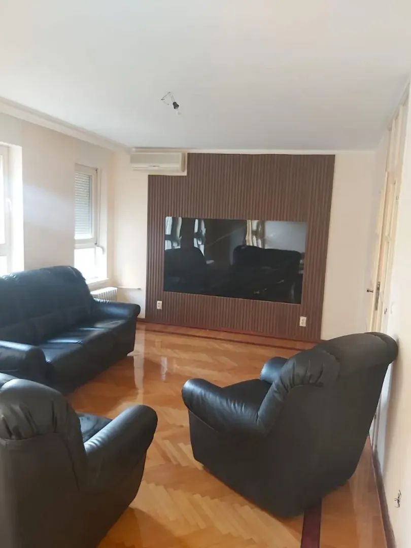 Dnevna soba sa crnim kožnim garniturama i parketom na podu.
