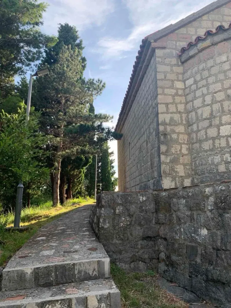 Eksterijer kamene kuće sa stazom i dvorištem okruženim zelenilom.